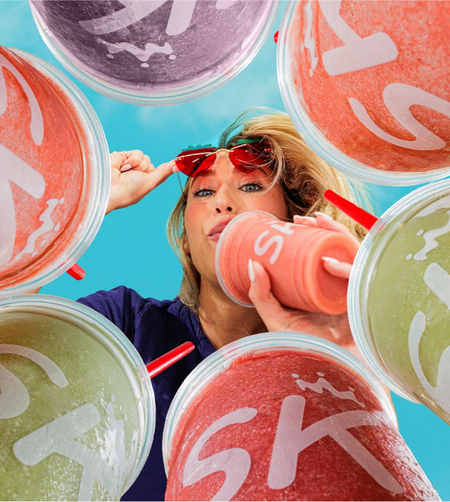 Woman looking down through a circle of smoothies lifting sunglasses while drinking a smoothie